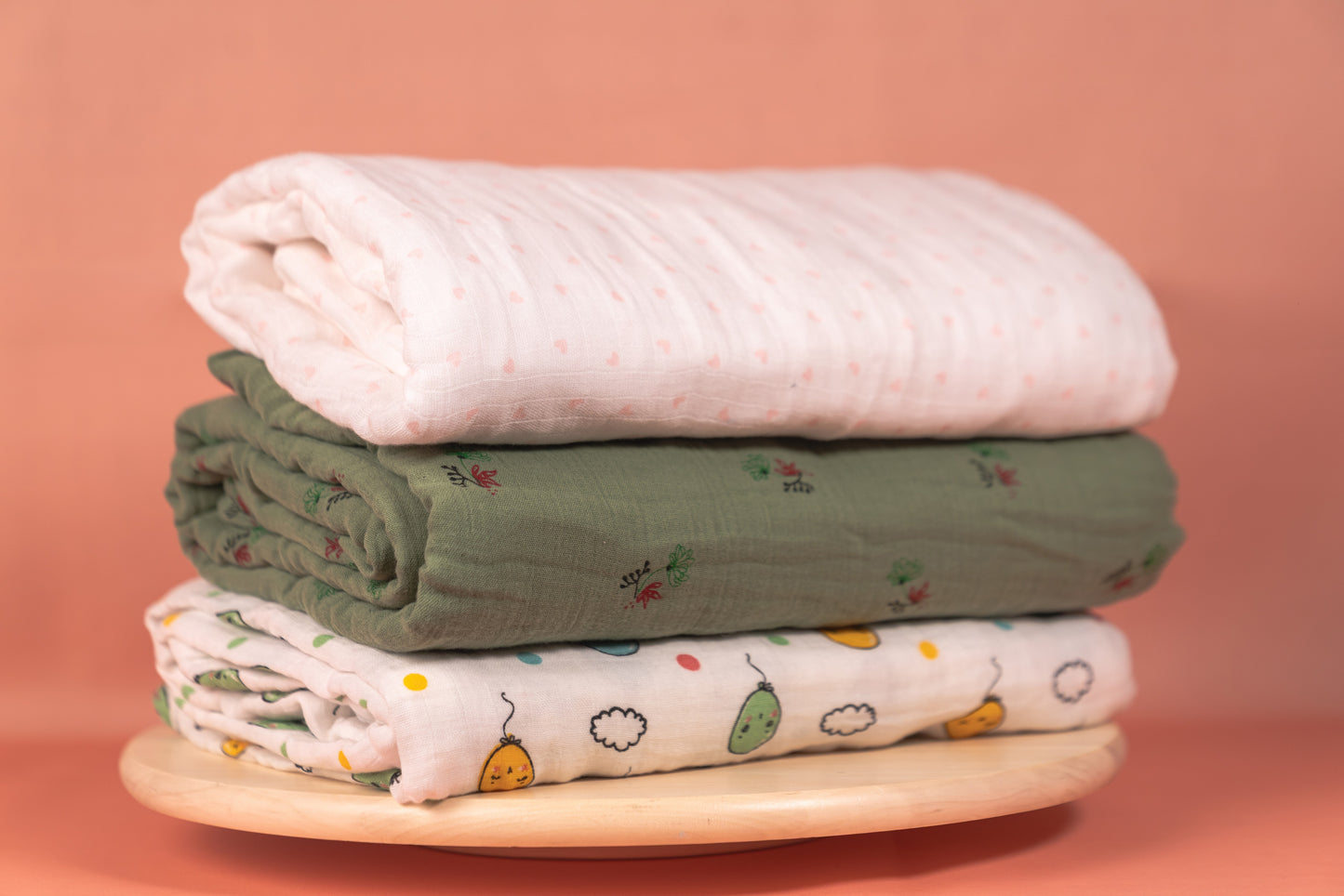 Stack of folded baby blankets on a wooden stand with a pink background