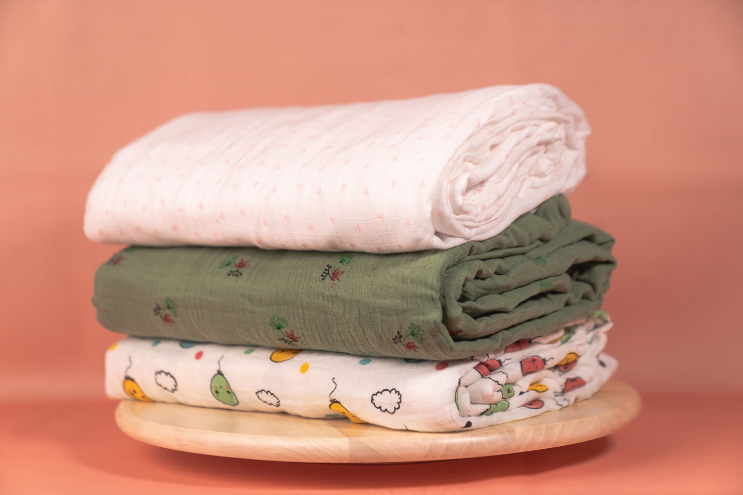 Stack of folded baby blankets on a wooden block against a pink background